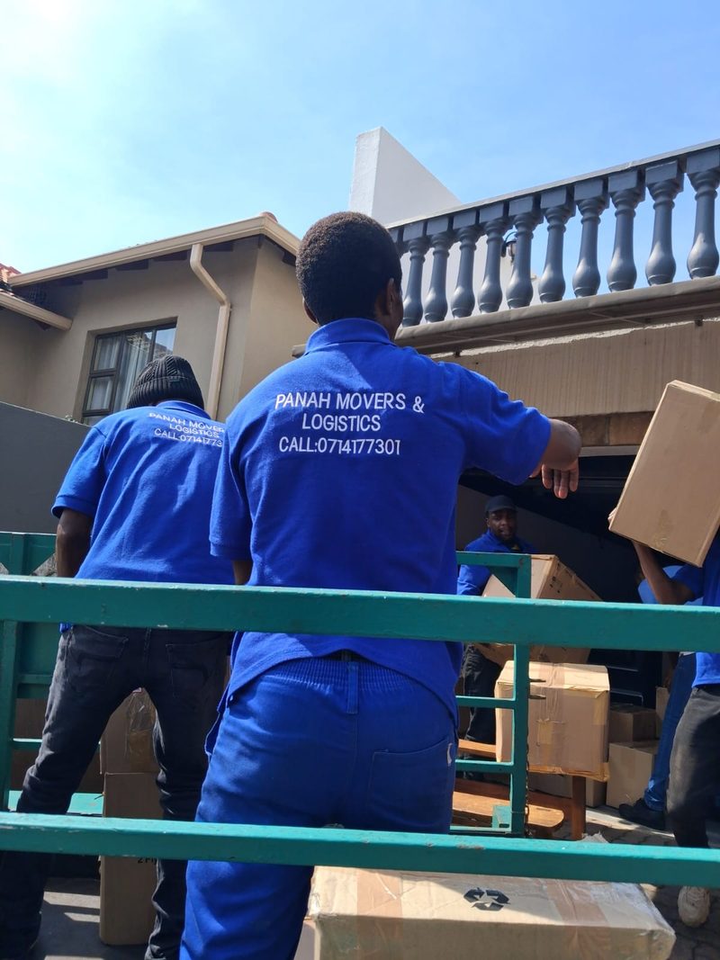 Crew in branded blue shirts printed with the company name and number, loading cartons and furniture from a house.