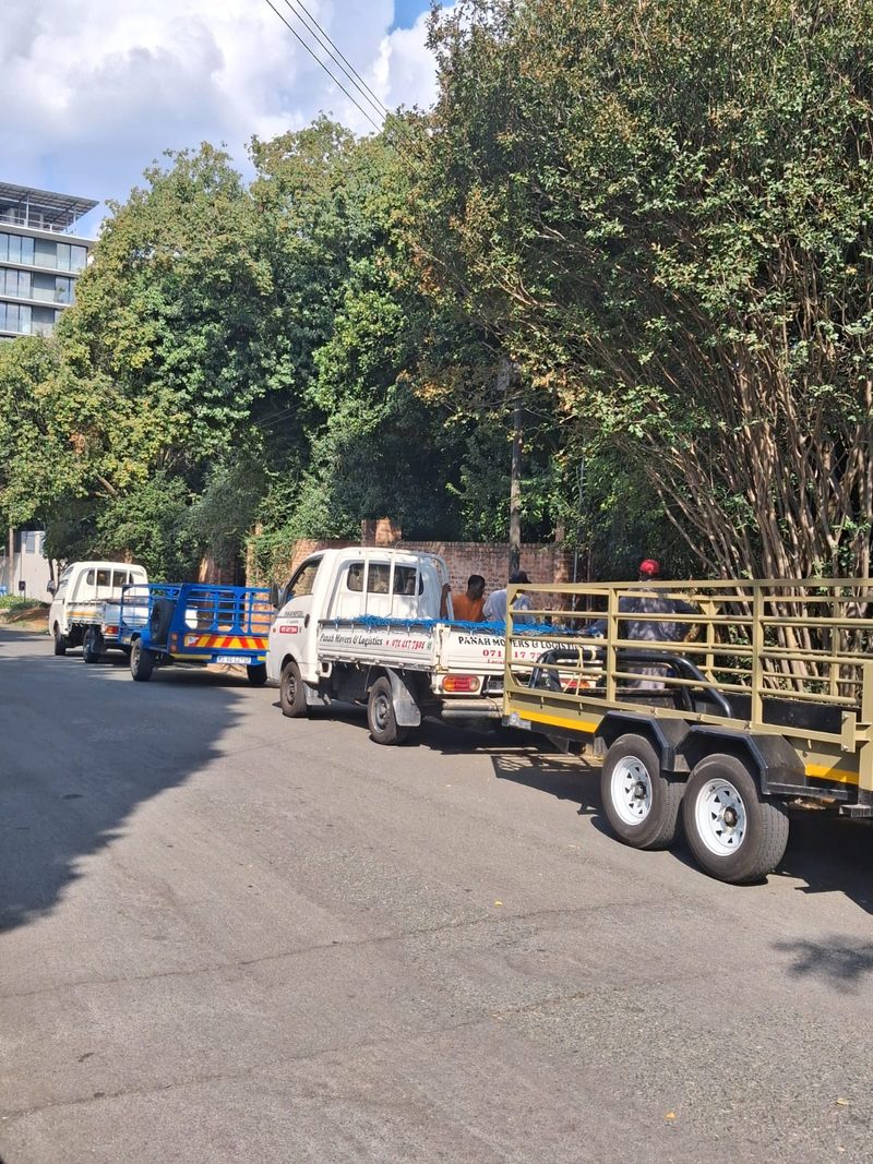 Two white Panah bakkies parked one behind the other on a tree-lined street, each with a trailer hitched.
