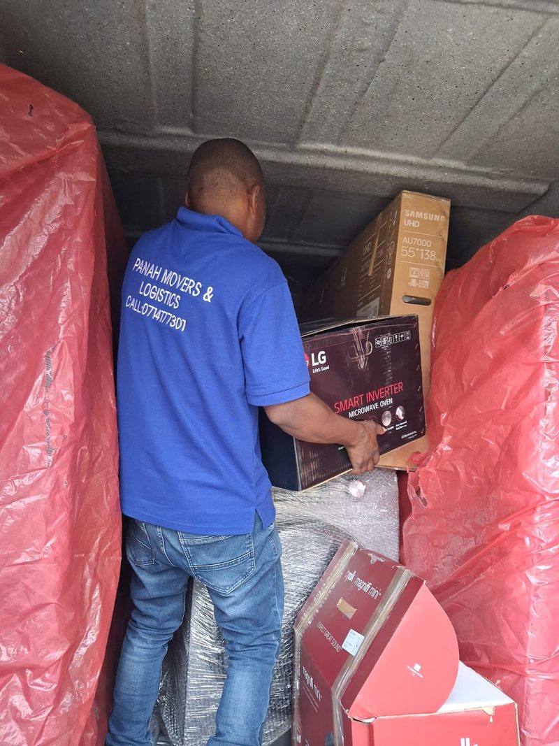 A crew member in a branded blue shirt stacking boxed appliances inside the covered load body of the bakkie.