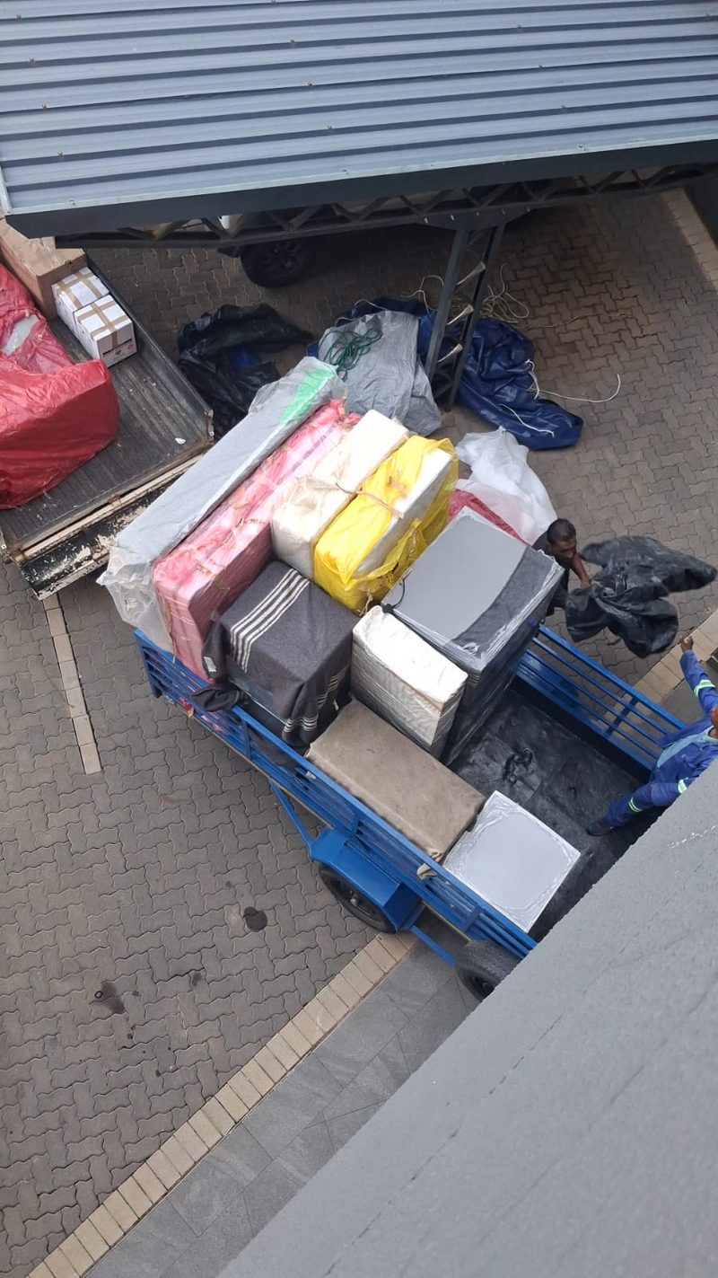 Looking down onto a loaded blue trailer packed with wrapped mattresses and bedding, with a crew member alongside.