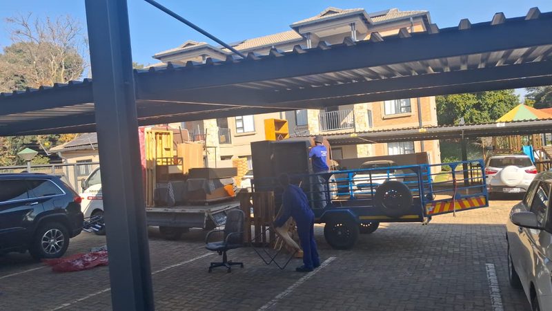 Crew loading furniture onto a trailer under a carport at a residential complex.