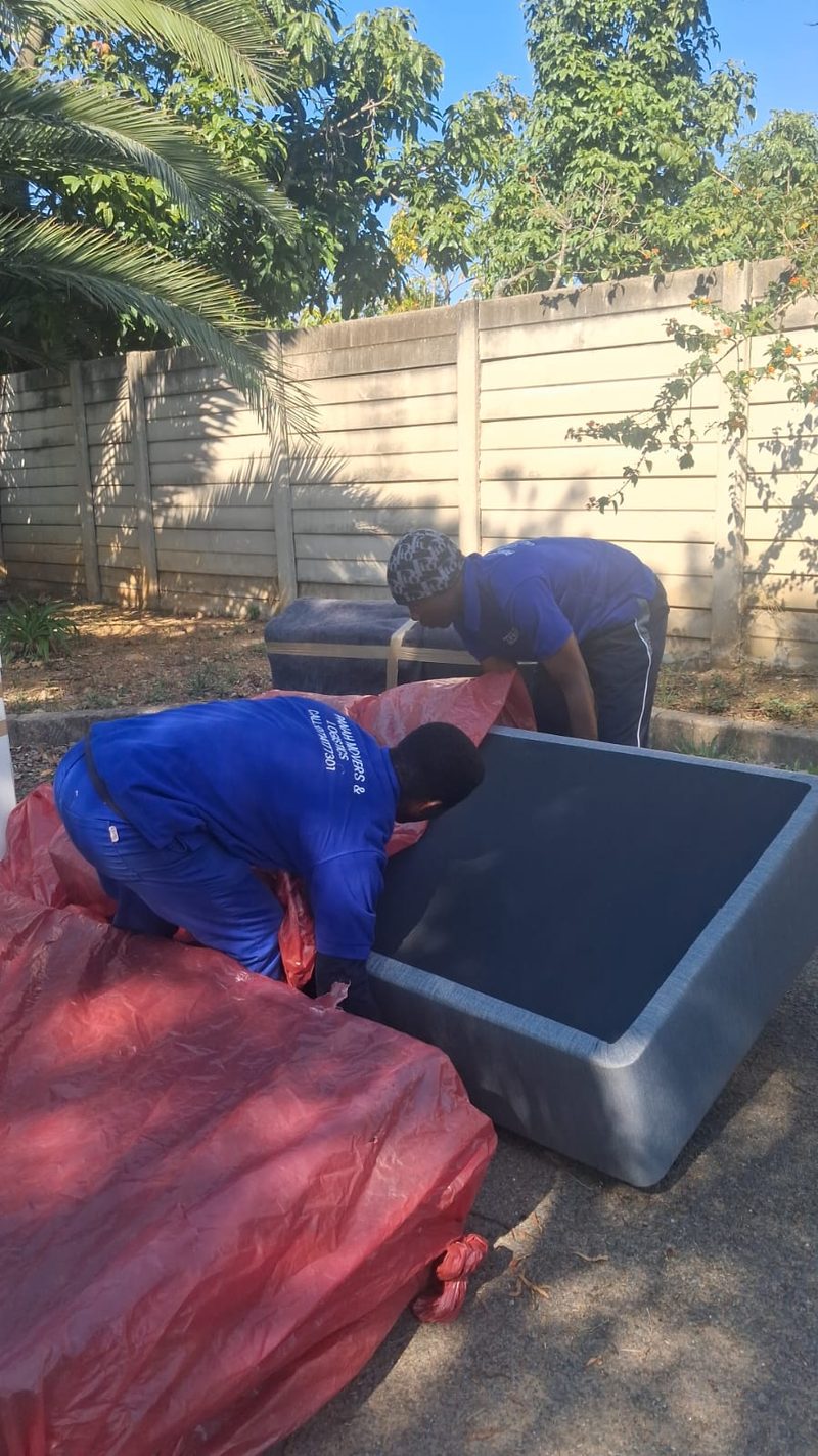 Two crew members in branded shirts covering a storage chest with red plastic sheeting in a yard.